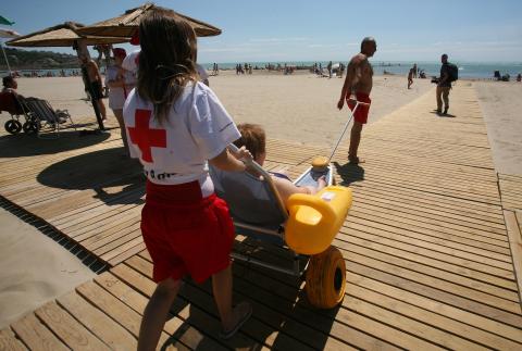 Una chica de la Cruz Roja con una silla accesible para el baño en una playa